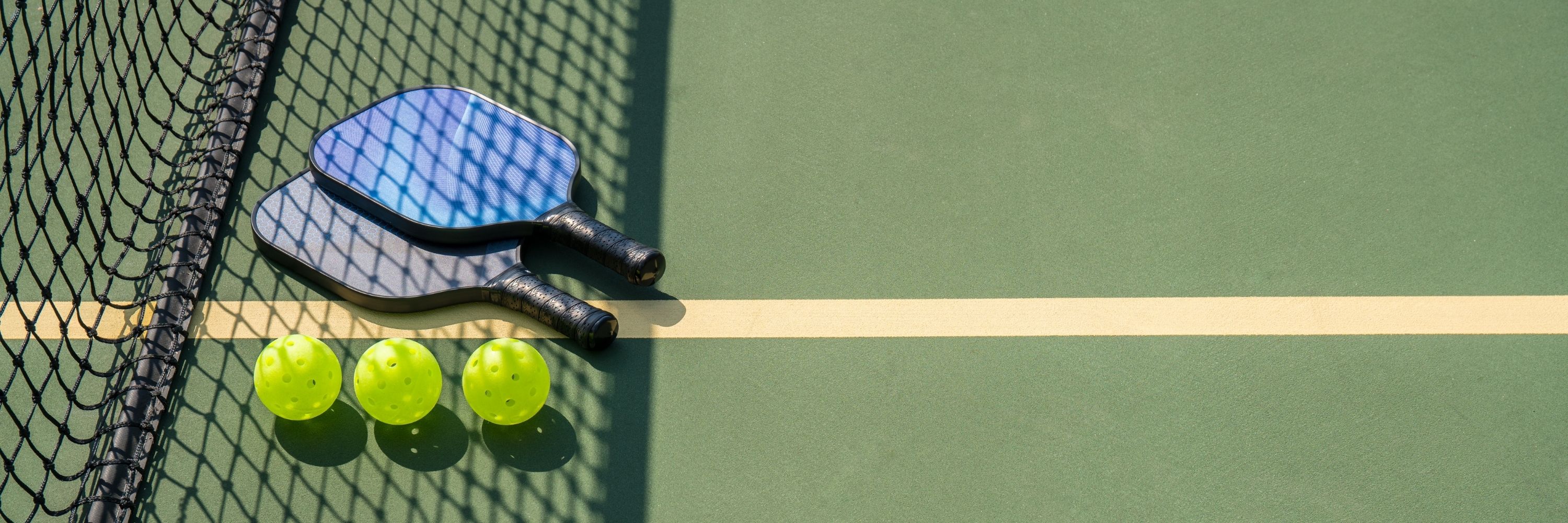 Pickleball Racquets And Balls On The Court Beside A Net