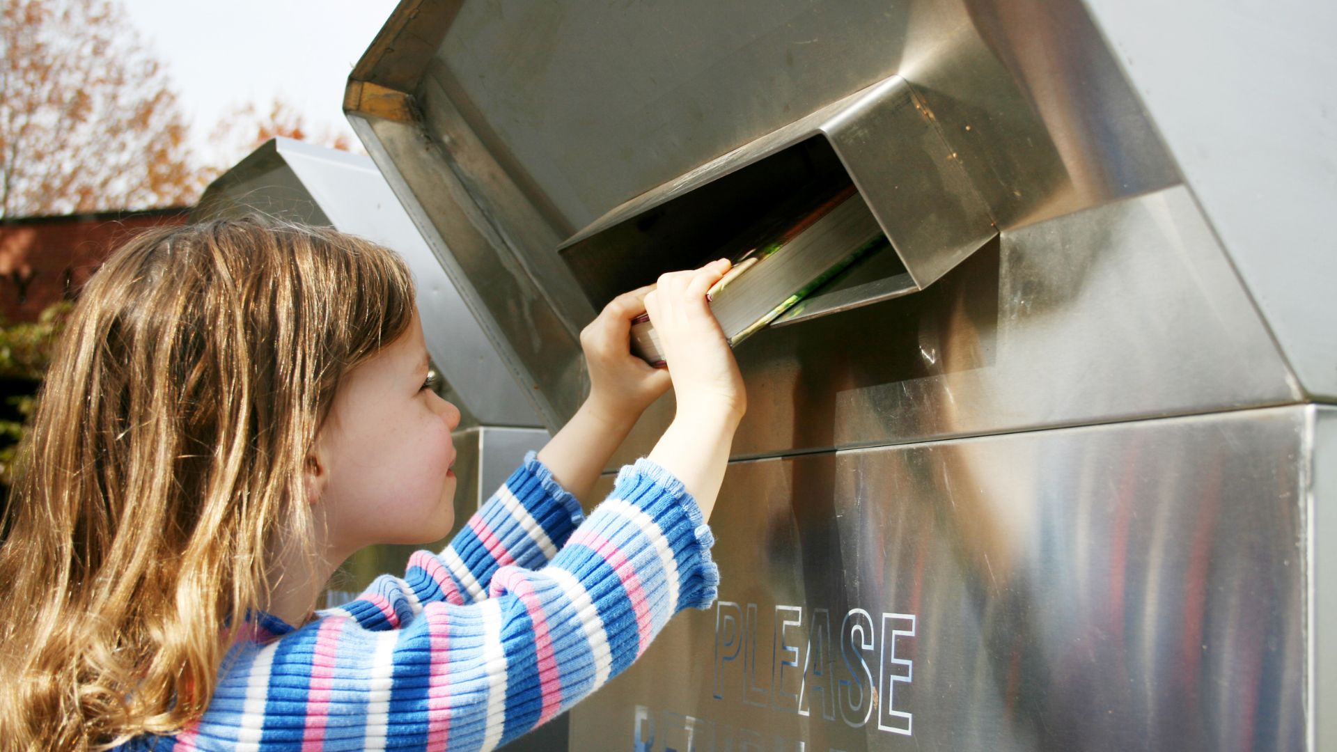 Little Girl Pushing Putting A Book Into The Book Return