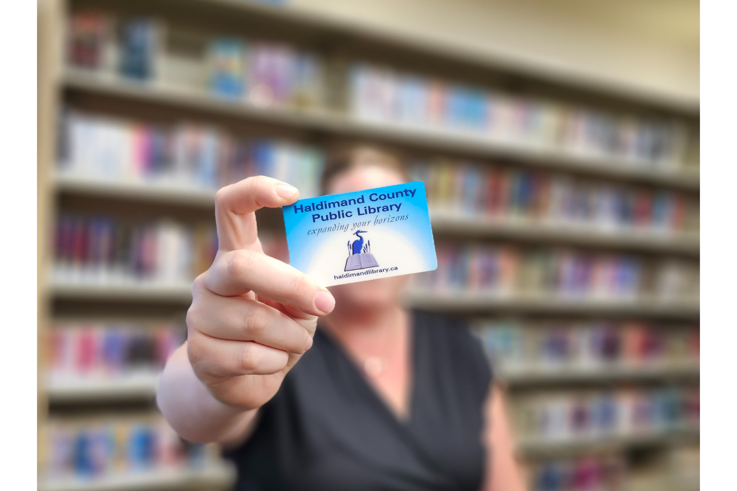 Blue and white library card being held up by woman in front of book shelves