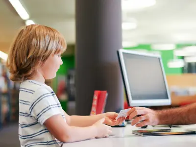 Little boy checking out a book with library card